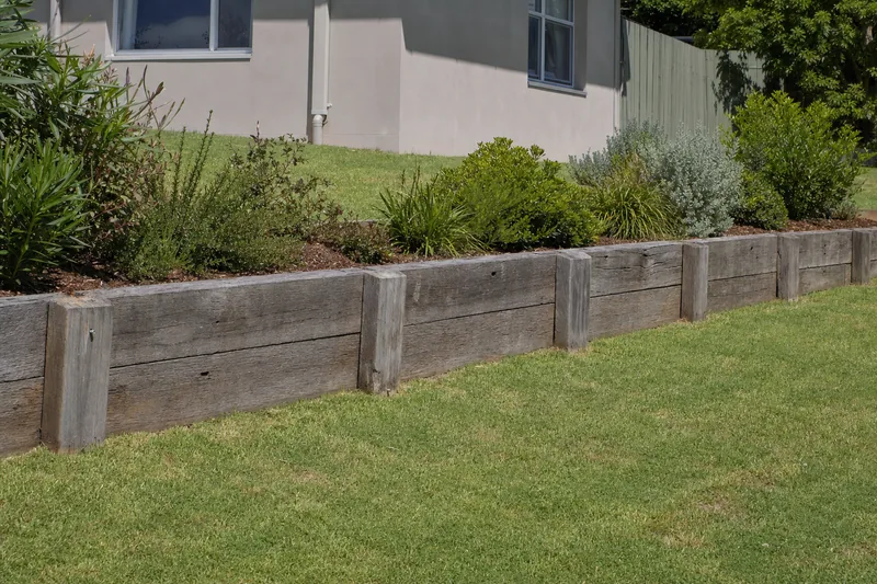 A finished timber sleeper retaining wall along a sloping backyard, with a garden bed planted above it — timber sleeper retaining wall, Gosford and the Central Coast. Illustrative example.